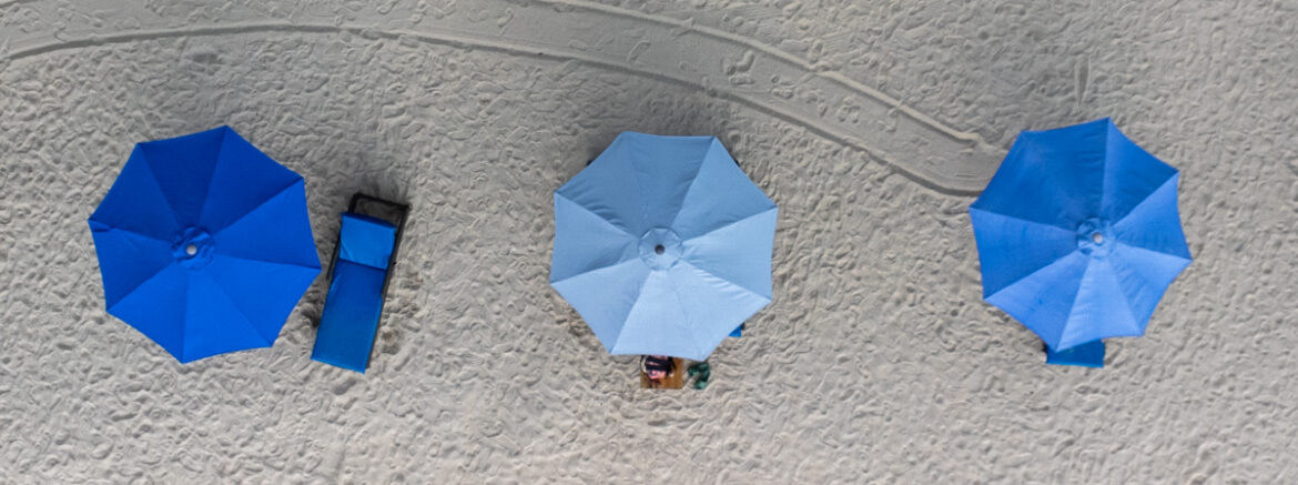 Trois parasols photographiés depuis au-dessus sur une plage de sable gris.