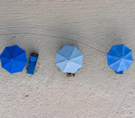 Trois parasols photographiés depuis au-dessus sur une plage de sable gris.